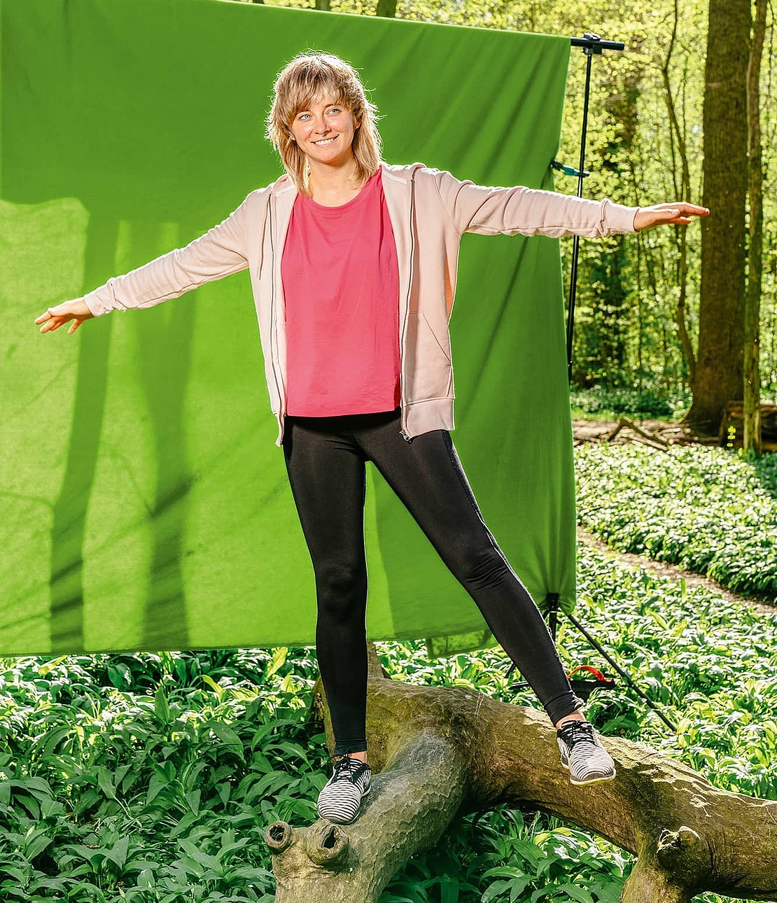 Frau balanciert im Wald auf Baumstamm vor grünem Hintergrund