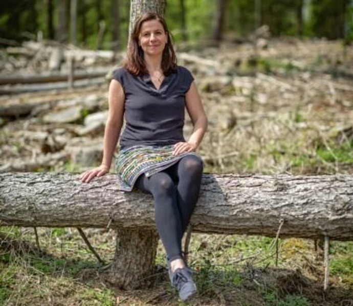 Frau sitzt im Wald auf einem Baumstamm