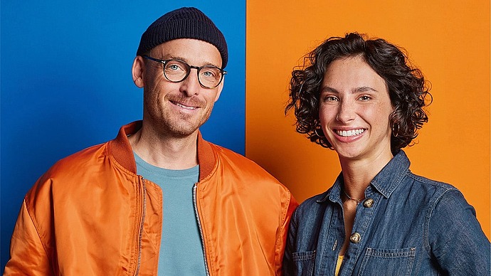 Zwei lächelnde Menschen stehen vor einem in Blau und Orange geteilten Hintergrund. Der Text lautet "Organspende - Ja oder nein?" und zeigt einen QR-Code mit Informationen zur Organspende in Deutschland.