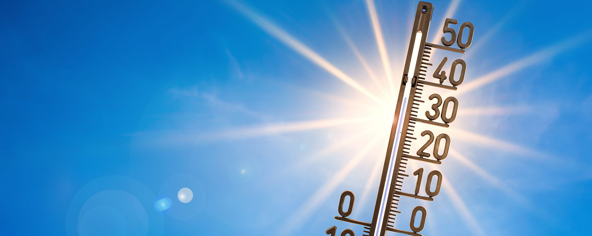 Ein Thermometer, das Temperaturen von über 30 °C anzeigt, steht vor einem strahlend blauen Himmel mit intensiver Sonneneinstrahlung und symbolisiert einen heißen, sonnigen Tag.