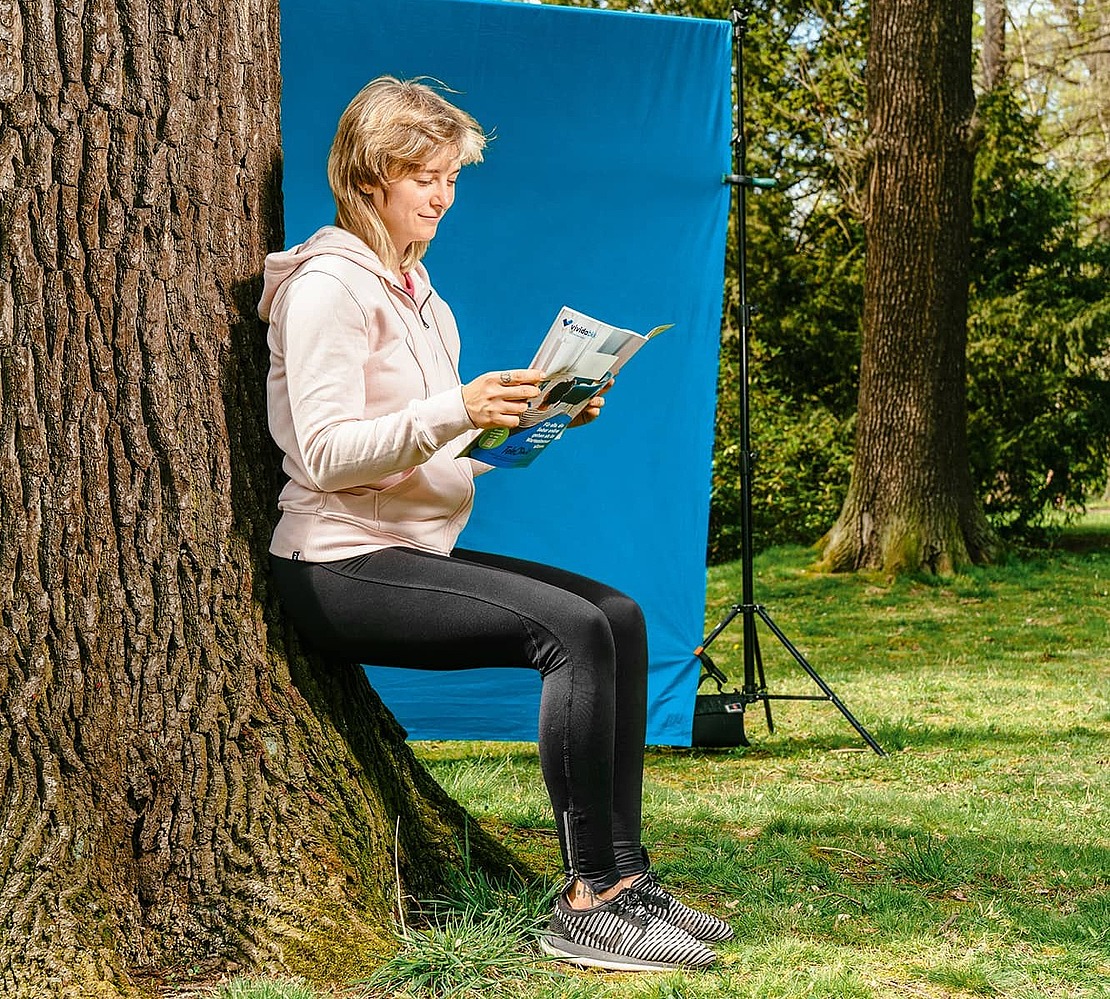 Frau lehnt sitzend an einem Baum und liest in einer Zeitschrift