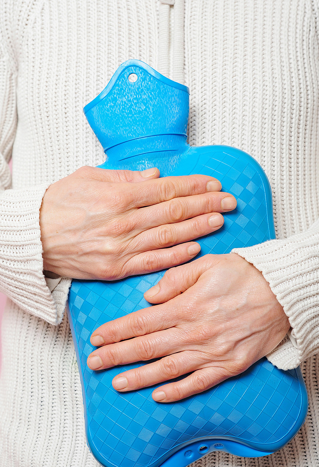 Eine Frau hält eine Wärmflasche an ihren Unterleib. Der Artikel behandelt das Thema Endometriose, das oft der Grund für starke Regelschmerzen ist.