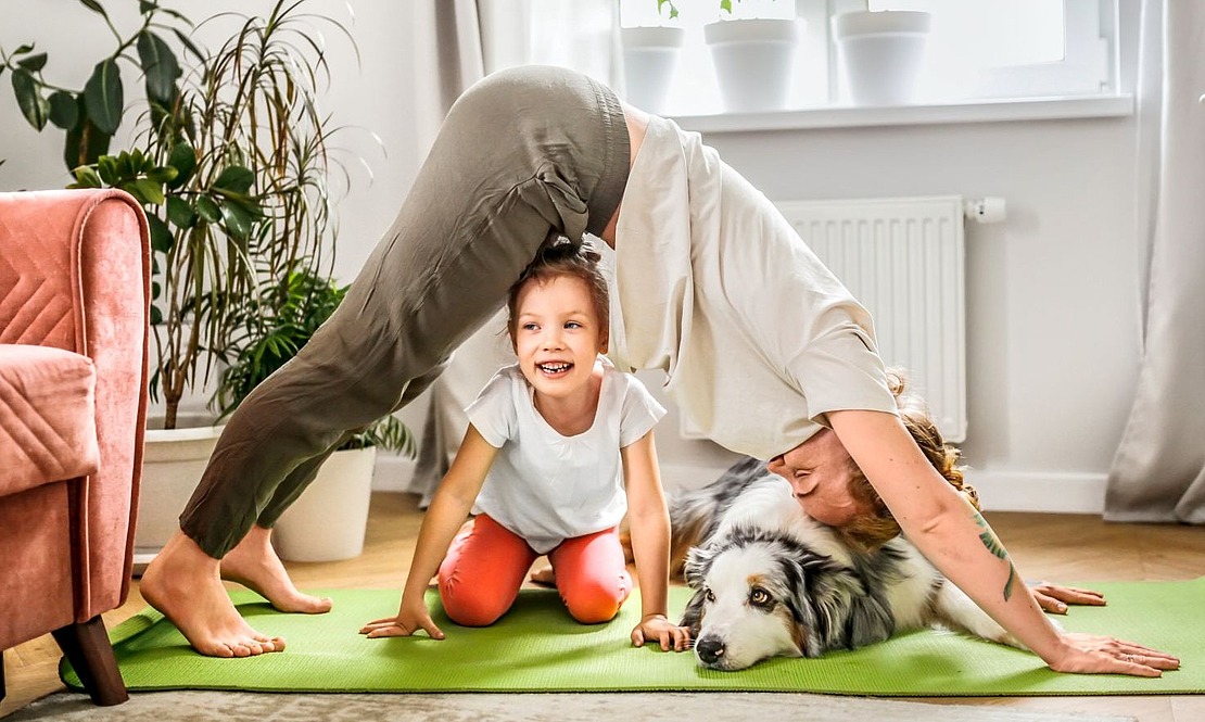 Frau macht Yoga, Kind und Hund sitzen dabei