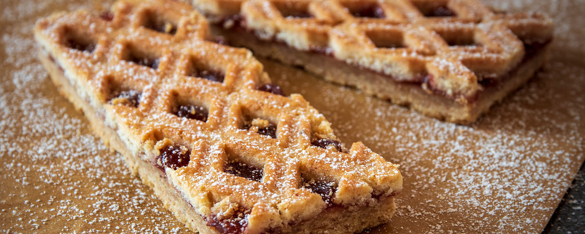 Rechteckige, mit Puderzucker bestäubte Blätterteigscheiben mit Fruchtfüllung, die auf braunem Pergamentpapier liegen.