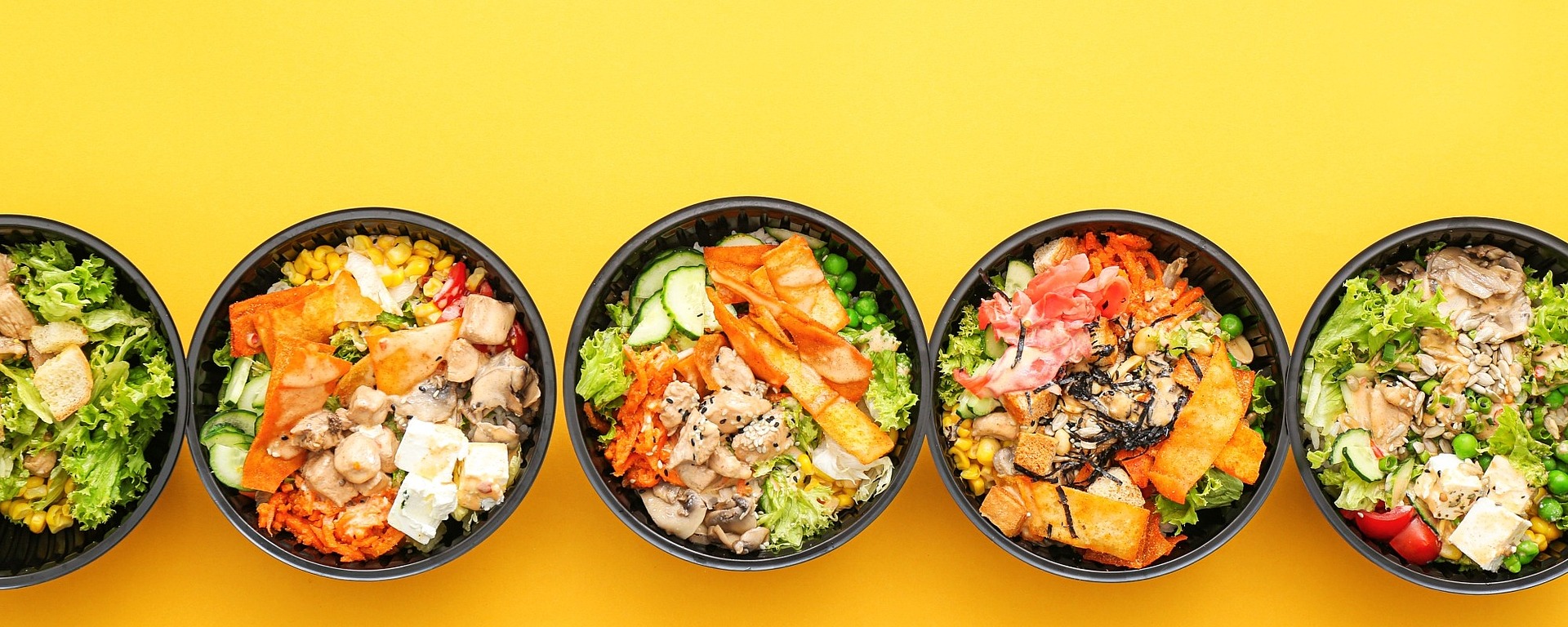 Fünf farbenfrohe Poke-Schalen mit verschiedenen Toppings, darunter Gemüse, Tofu und Seetang, sind in einer Reihe vor einem leuchtend gelben Hintergrund angeordnet.