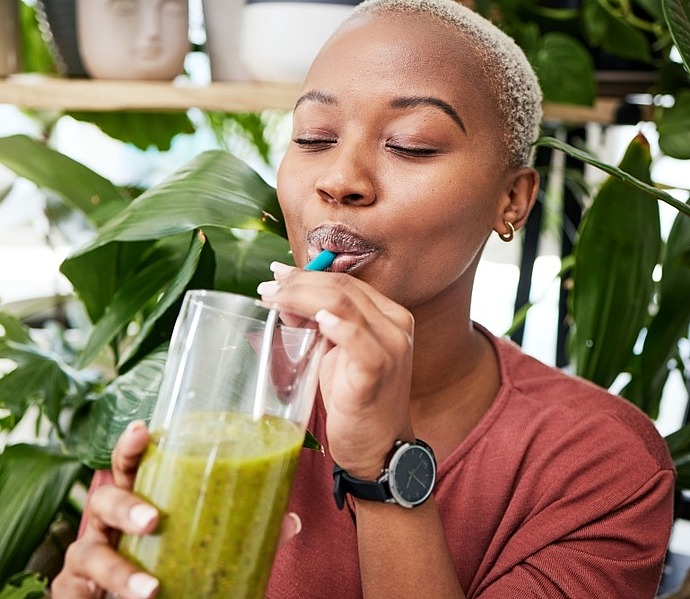 Eine Person genießt einen grünen Smoothie mit einem Strohhalm aus einem Glas.