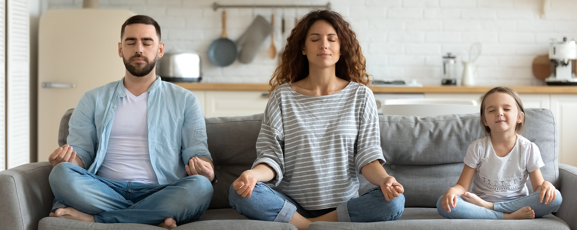 Familie sitzt auf dem Sofa im Schneidersitz mit geschlossenen Augen