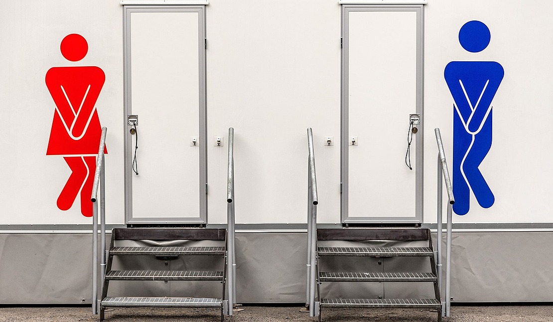 Zwei Toilettentüren mit Treppen; eine hat ein rotes weibliches Symbol und die andere ein blaues männliches Symbol, beide mit gekreuzten Beinen, die die Dringlichkeit anzeigen.