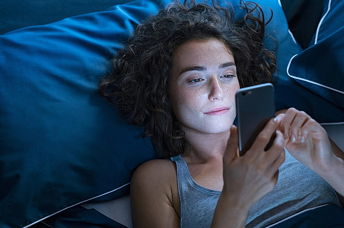 Frau liegt mit Smartphone nachts im Bett