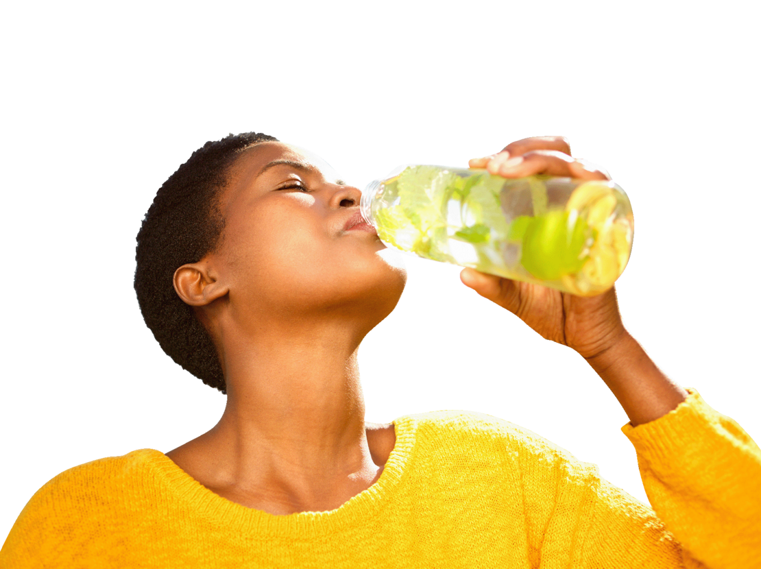 Eine Person in einem gelben Pullover trinkt vor einem weißen Hintergrund Wasser aus einer durchsichtigen Flasche mit Zitronenscheiben und Kräutern.