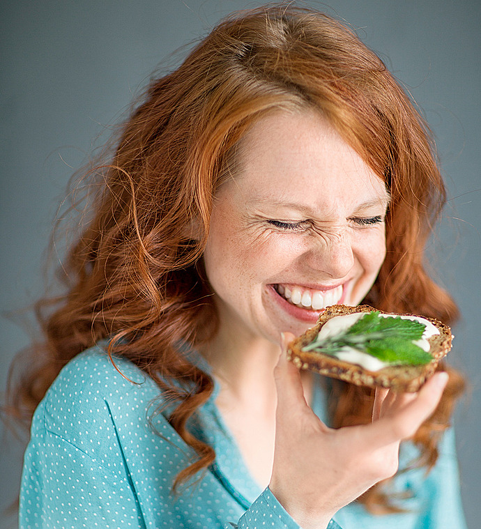 Eine lachende Frau mit einer Scheibe Körnerbrot in der Hand. Im Text geht es um intuitives Essen und die intuitive Ernährung.